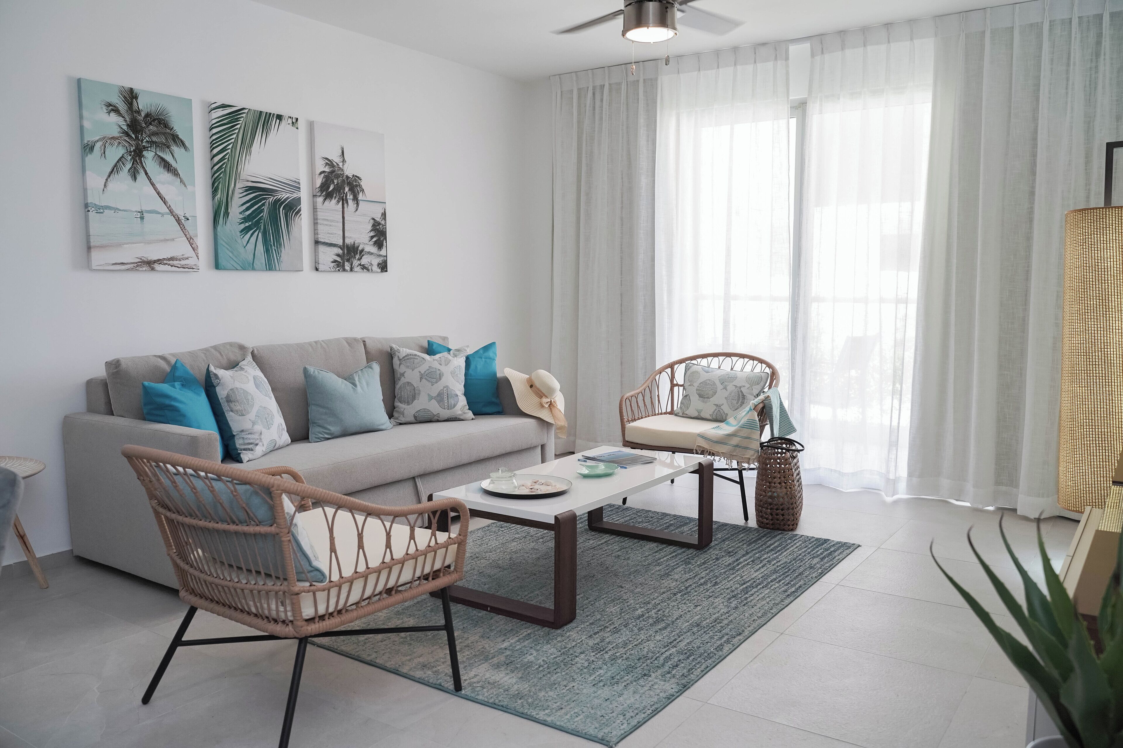 Ein modernes Wohnzimmer mit einer Couch, zwei Korbstühlen, einem Couchtisch und einem großen Fenster mit durchscheinenden Vorhängen.