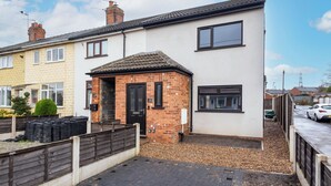 A two-story residential building with a brick extension, a front door, and a small garden area with a wooden fence.