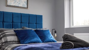 A bedroom with a blue headboard, striped bedding, and a rolled towel on the bed.