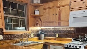 Una cocina con gabinetes de madera, encimera de granito, pileta, estufa y taburetes de bar.