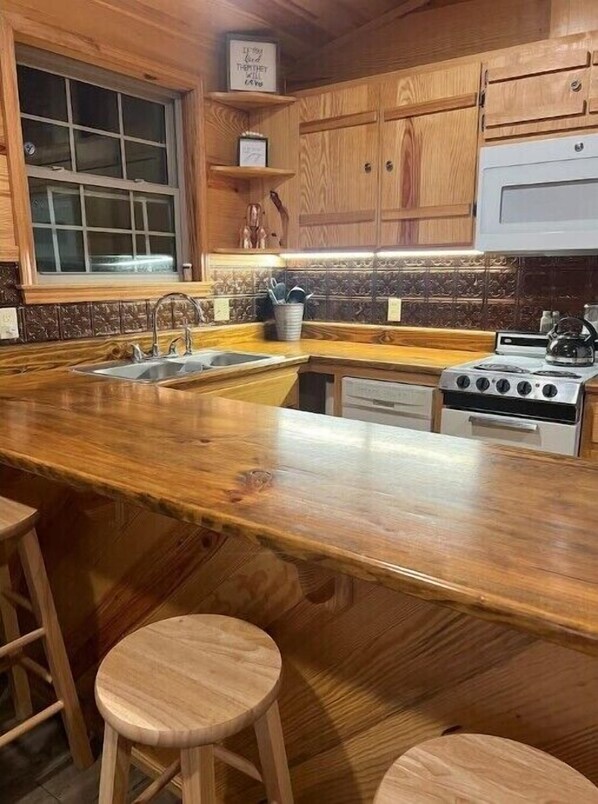A kitchen with wooden cabinets, a granite countertop, a sink, a stove, and bar stools.