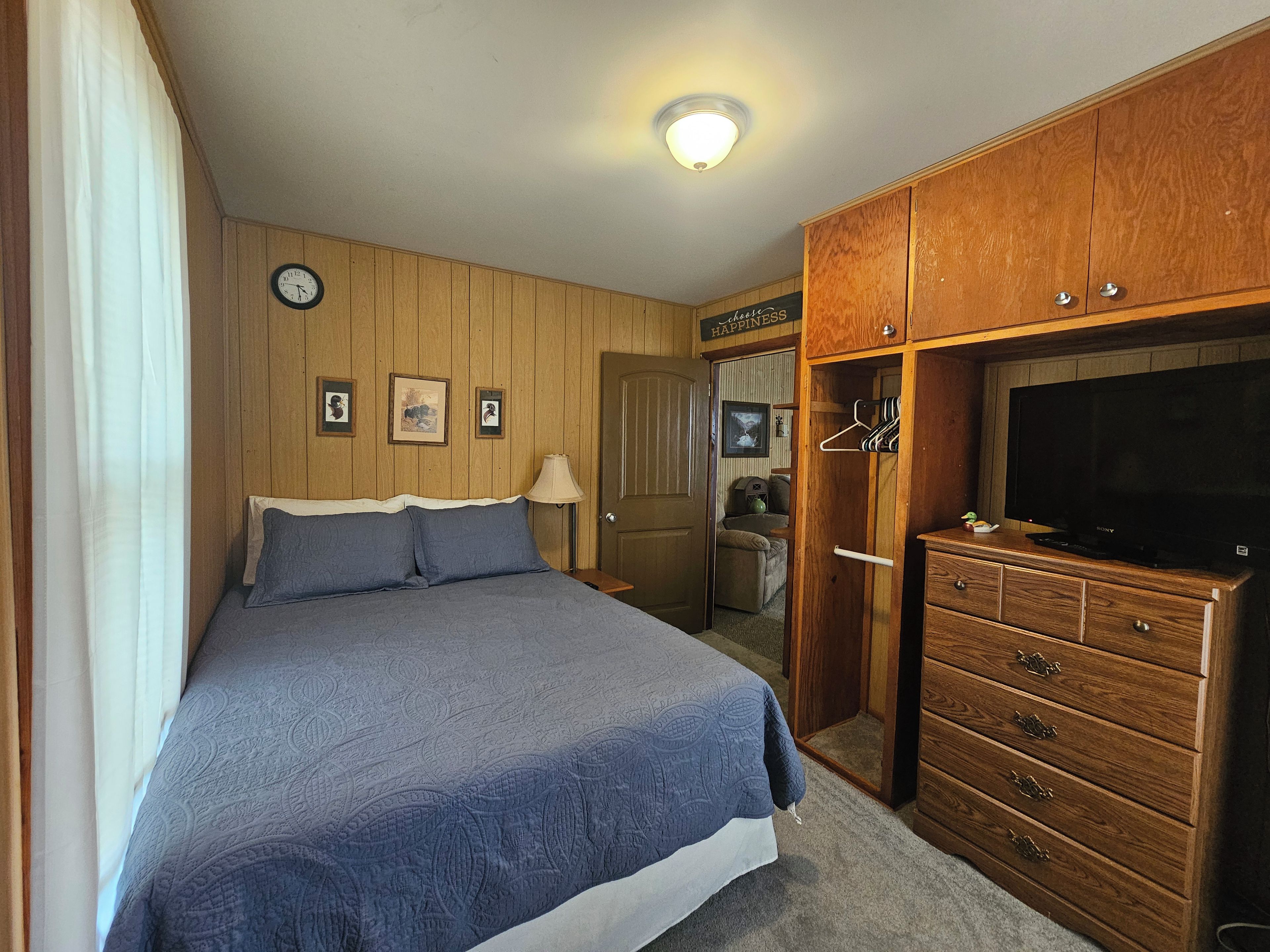Une chambre à coucher comprenant un lit, une commode, un téléviseur et une porte donnant sur une autre pièce.