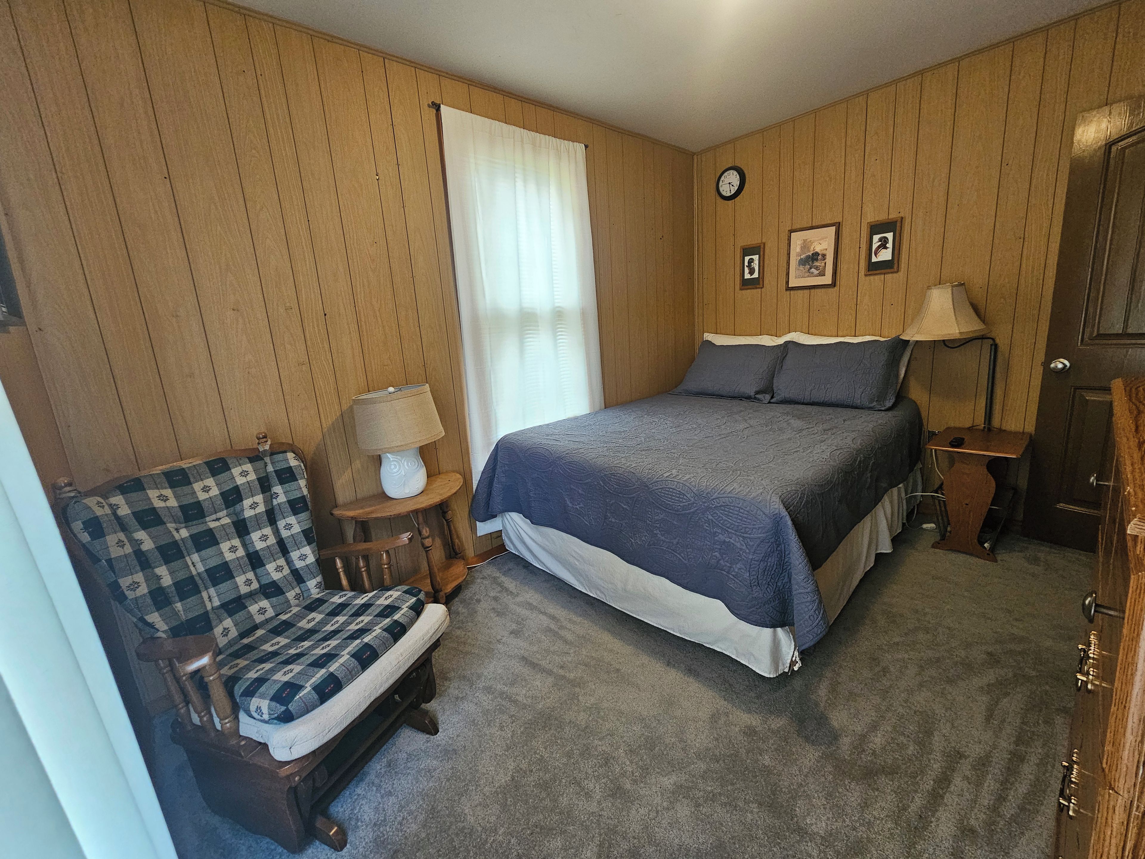 A bedroom with a bed, a chair, a lamp, and a clock on the wall.