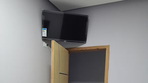 A bedroom with a bed, a television mounted on the wall, and a door leading to another room. - ITIS HOTEL (Dom Eliseu)
