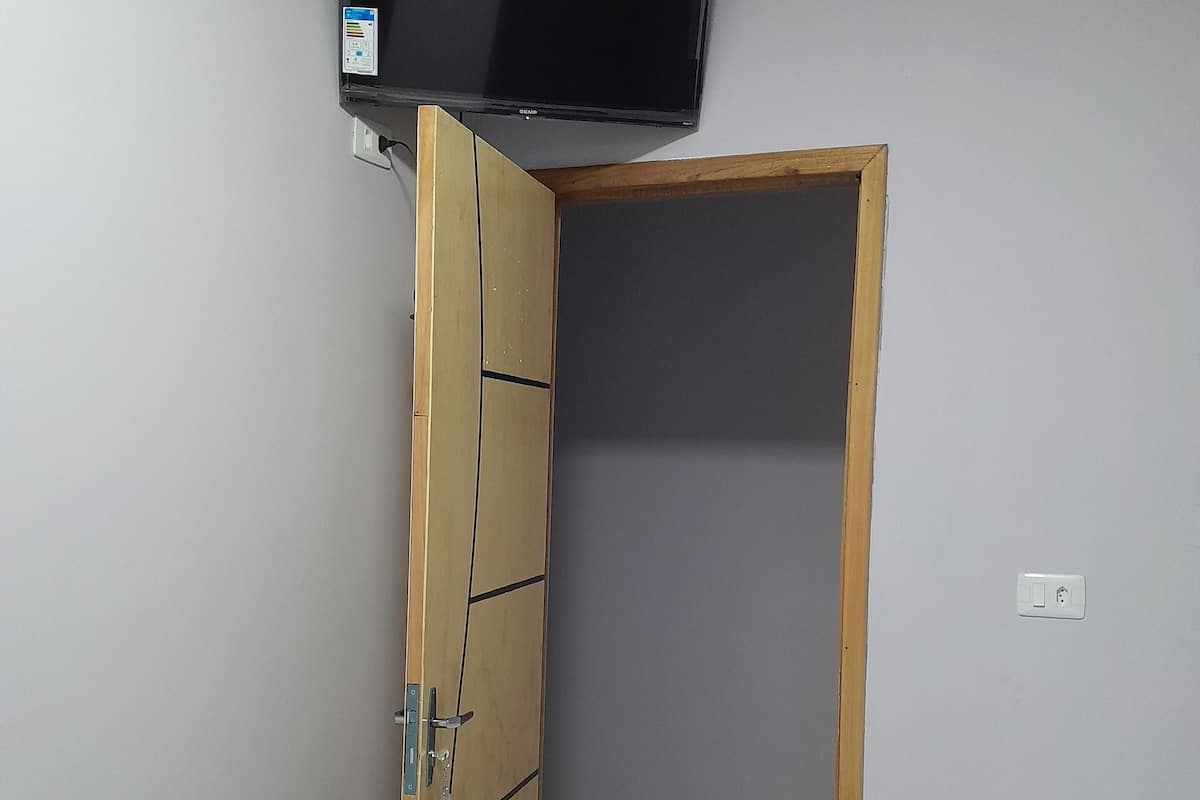 Une chambre à coucher avec un lit, un téléviseur fixé au mur et une porte donnant sur une autre pièce.
