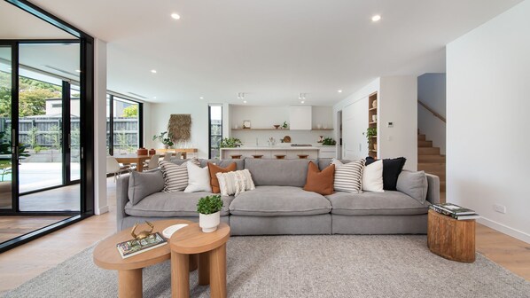 Ein modernes Wohnzimmer mit einem grauen Ecksofa, einem Couchtisch und einem Essbereich mit Holztisch und Stühlen.