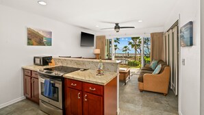 A modern kitchen with a large island, a dining area with a view, and a living room with a sofa. - 3 Bedroom Ocean Front Condo with Pool & Elevator! (Kapaʻa)