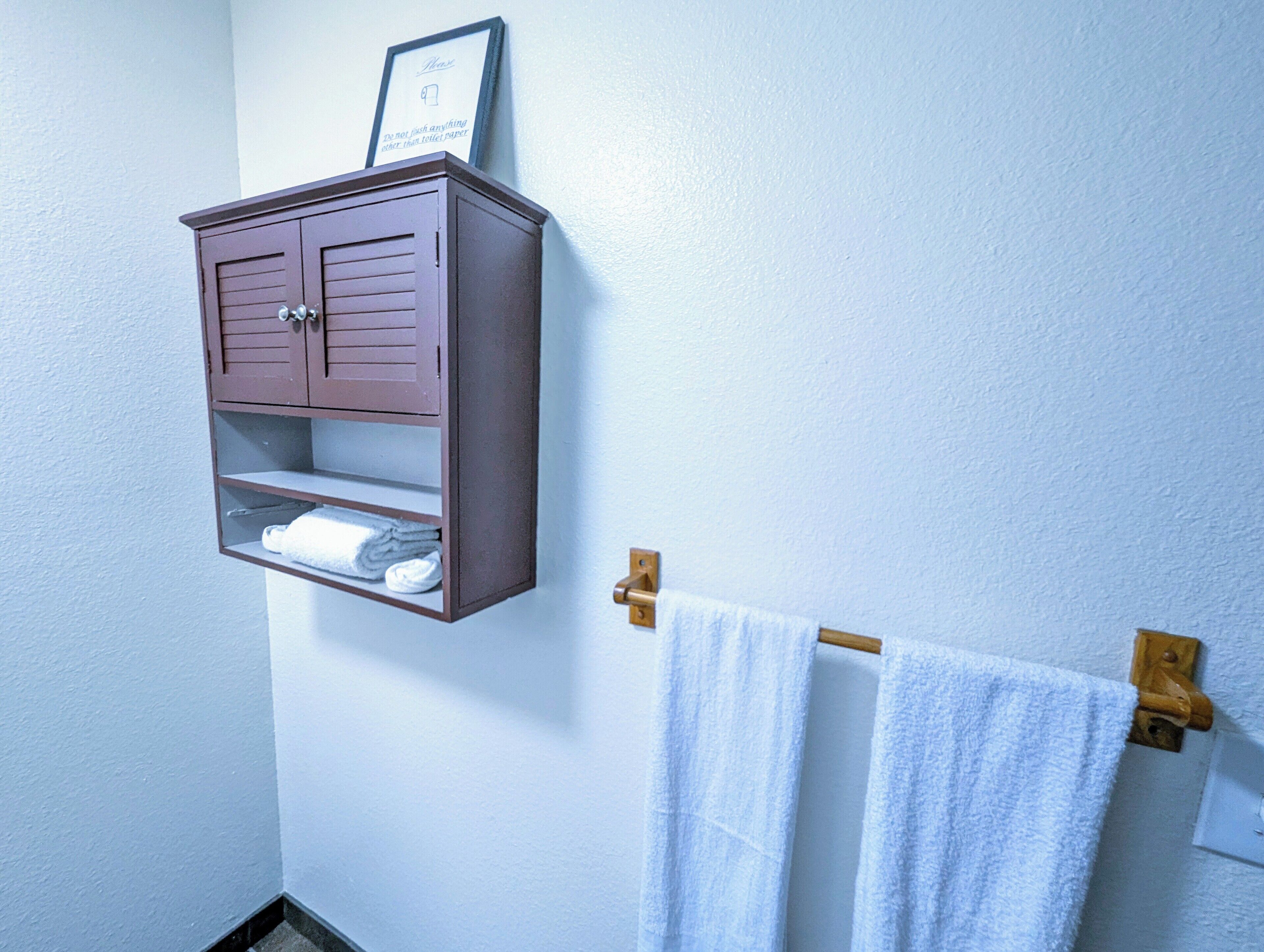 Un baño con un mueble de madera, un perchero y un cartel en la pared.