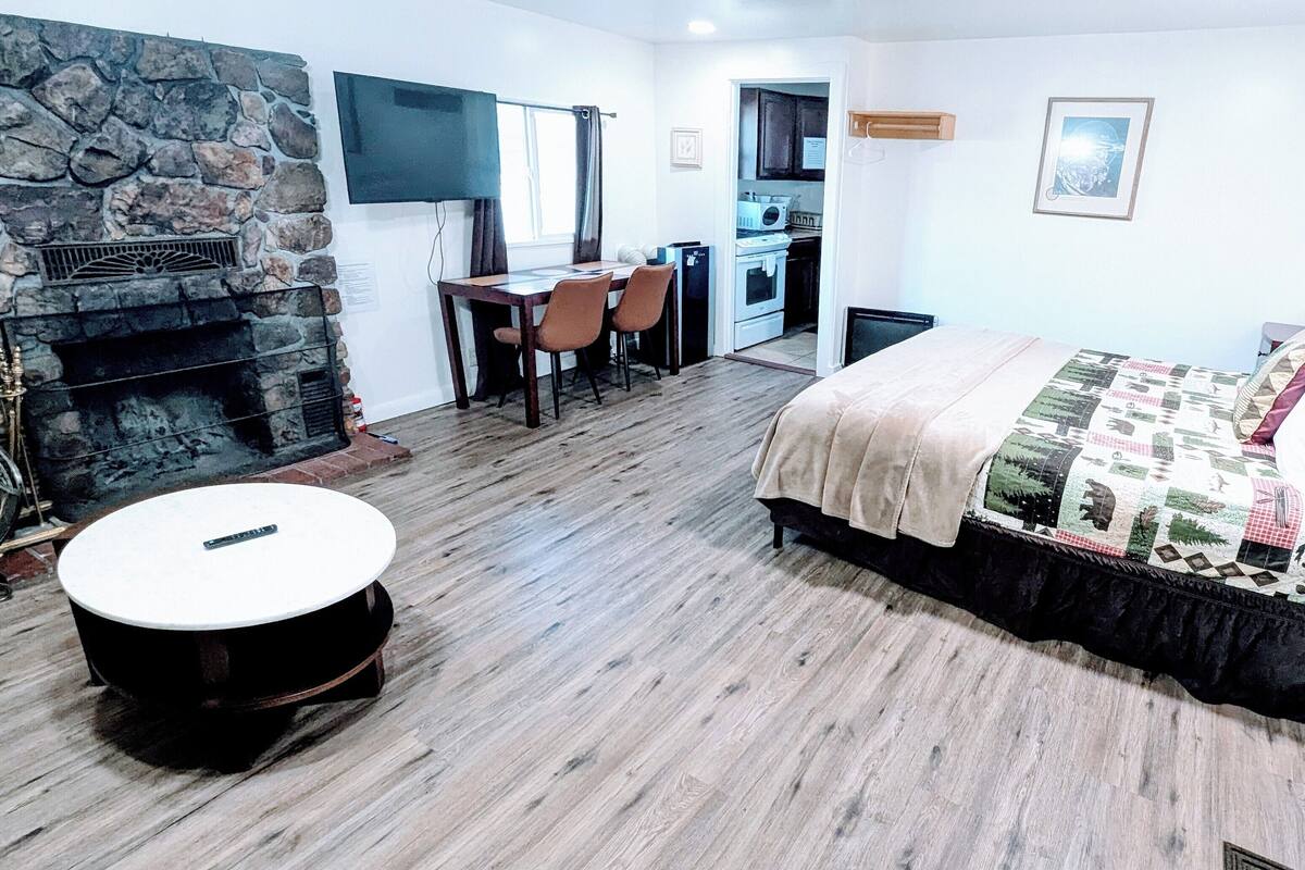 Une chambre avec un lit, une table ronde, une cheminée, un coin cuisine et une table à manger avec des chaises.