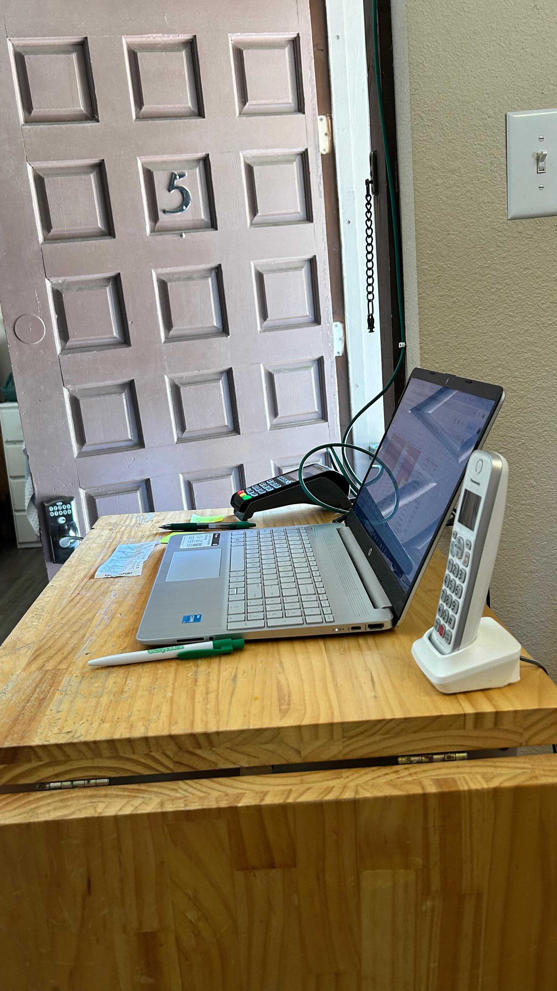 A wooden desk with a laptop, a pen, a remote control, and a telephone.