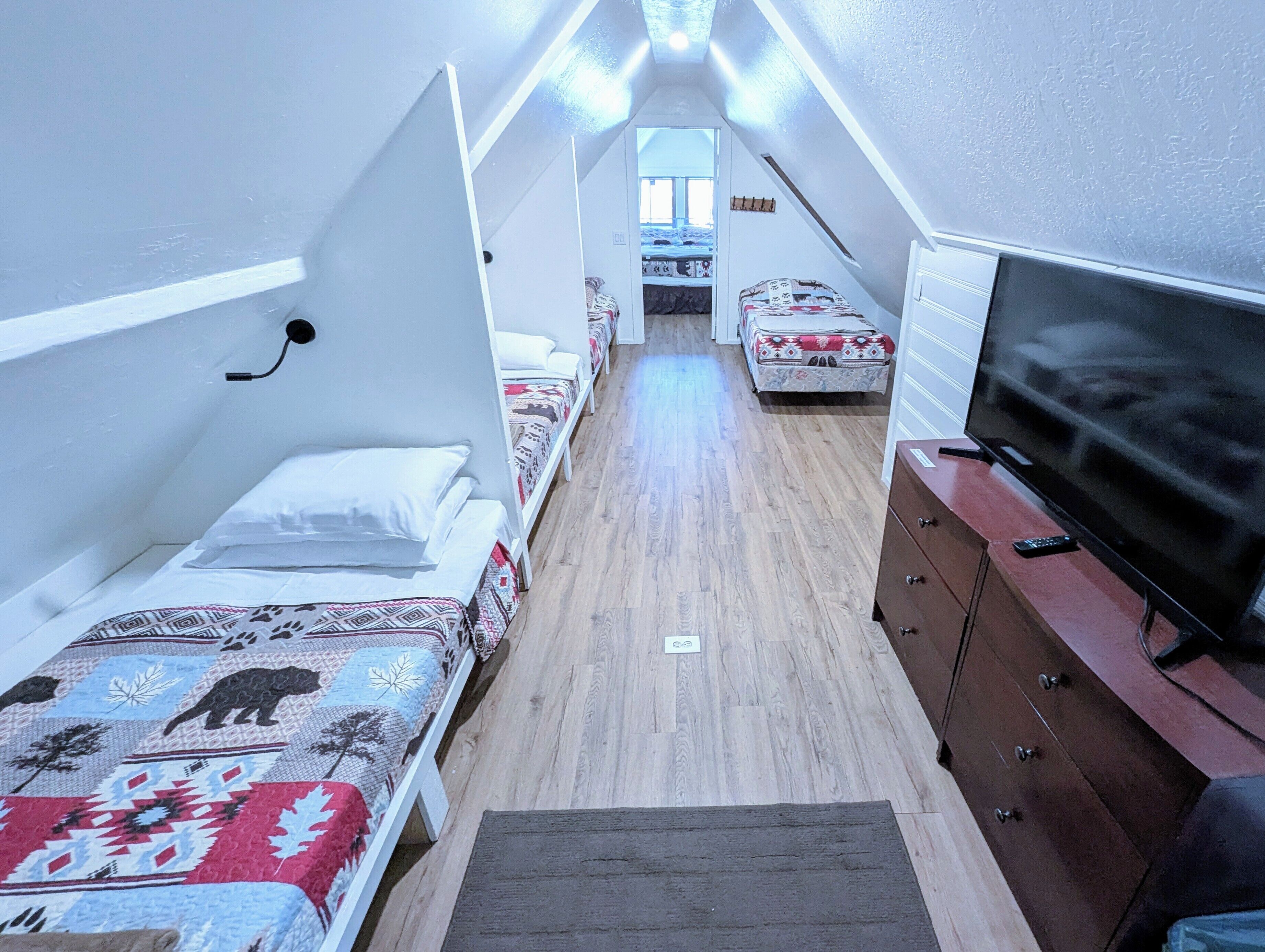 Ein schmales, gut beleuchtetes Zimmer mit zwei Betten, einem Fernseher und einer Kommode.
