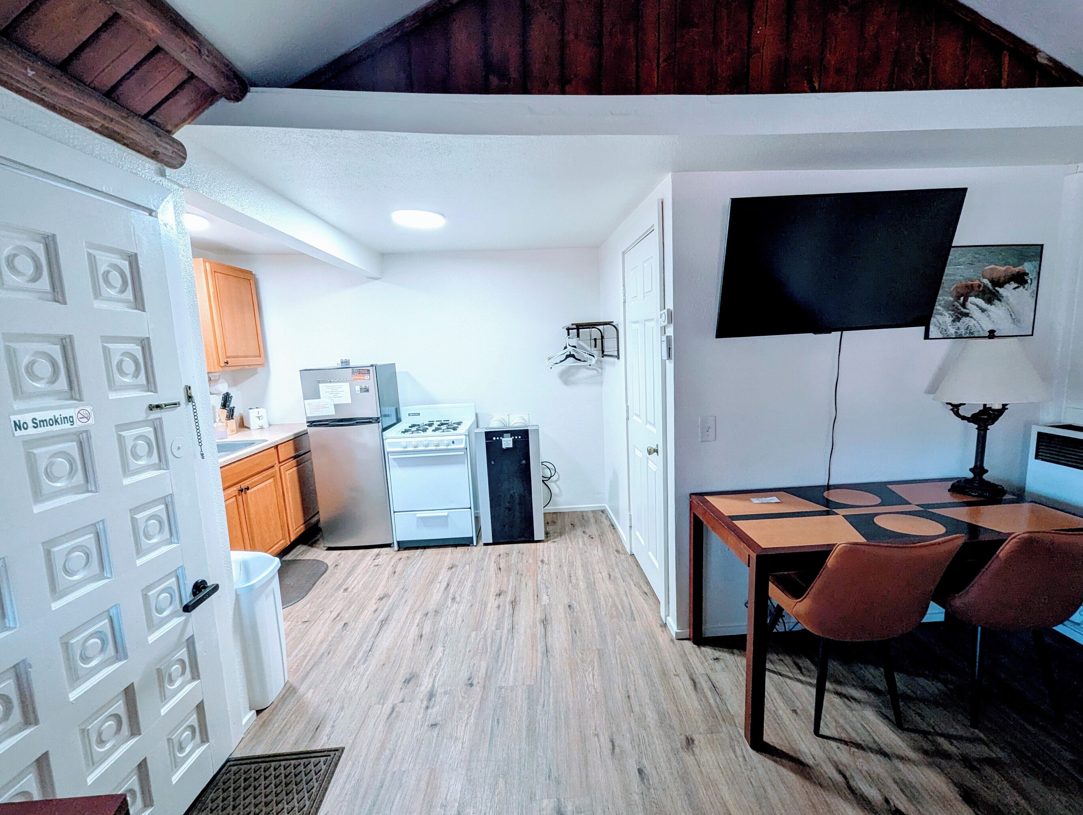A compact kitchen with a refrigerator, stove, and microwave. There's a dining table with chairs and a TV mounted on the wall.