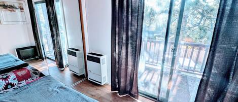 A room with a bed, a TV, a heater, and a large window with curtains.
