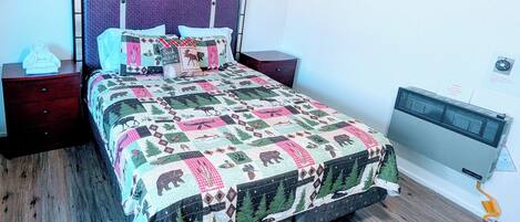 A bed with a quilt featuring wildlife patterns, a headboard with a grid design, and a wall-mounted air conditioner.