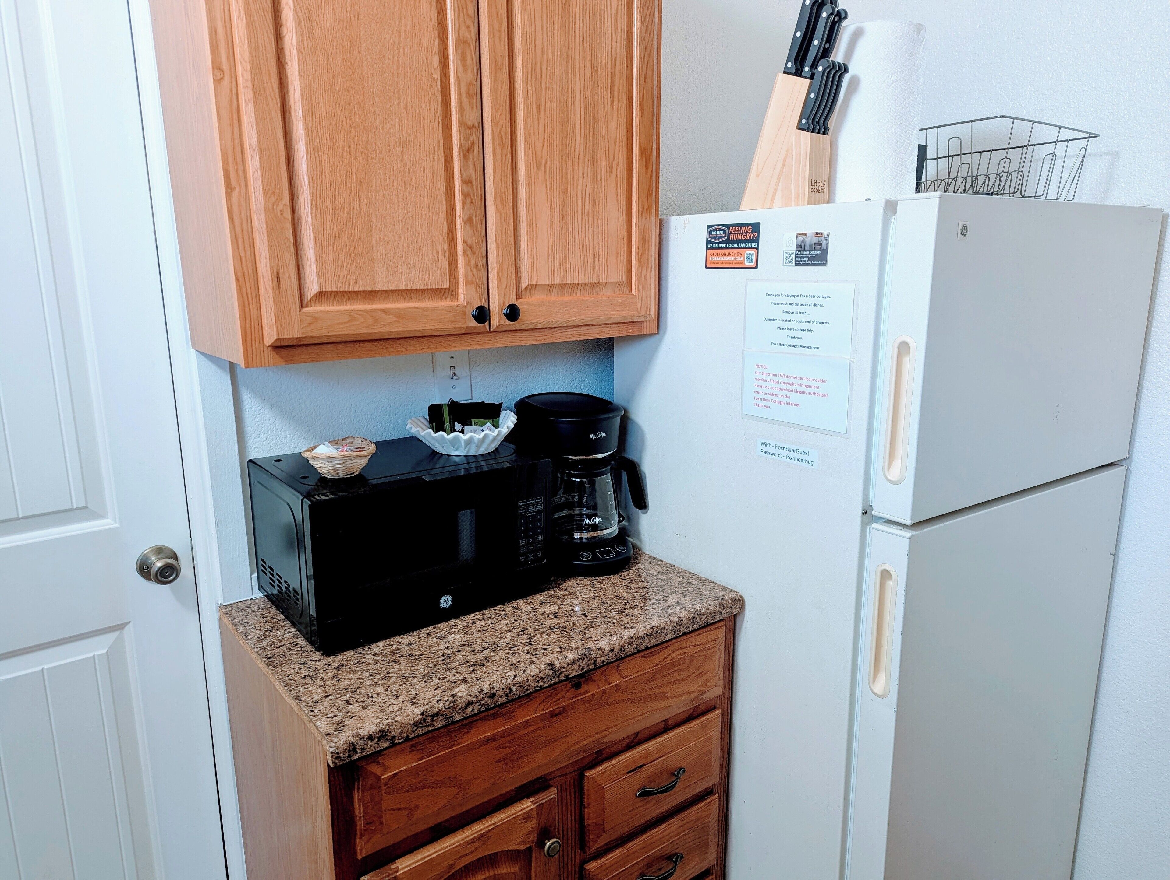 A compact kitchen with wooden cabinets, a black microwave, a white refrigerator, and a coffee maker.