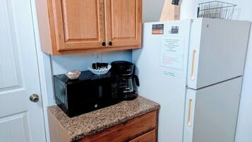 A compact kitchen with wooden cabinets, a black microwave, a white refrigerator, and a coffee maker.