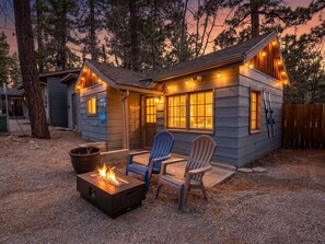 Una cabaña con un brasero, dos sillas Adirondack y una terraza.