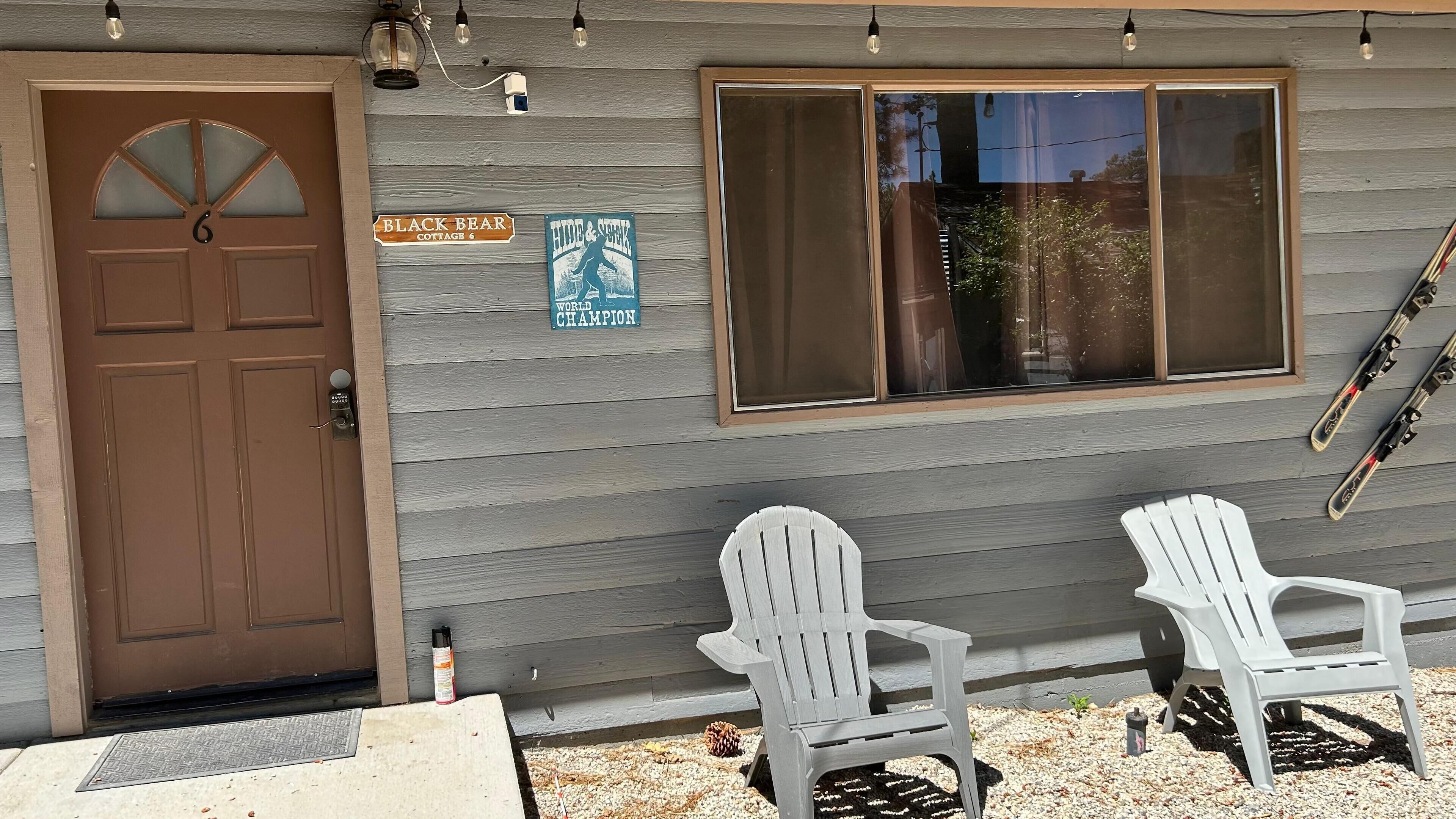 A wooden cottage with a brown door, two Adirondack chairs, a window, and a sign indicating it's a 'World Champion' ski resort.