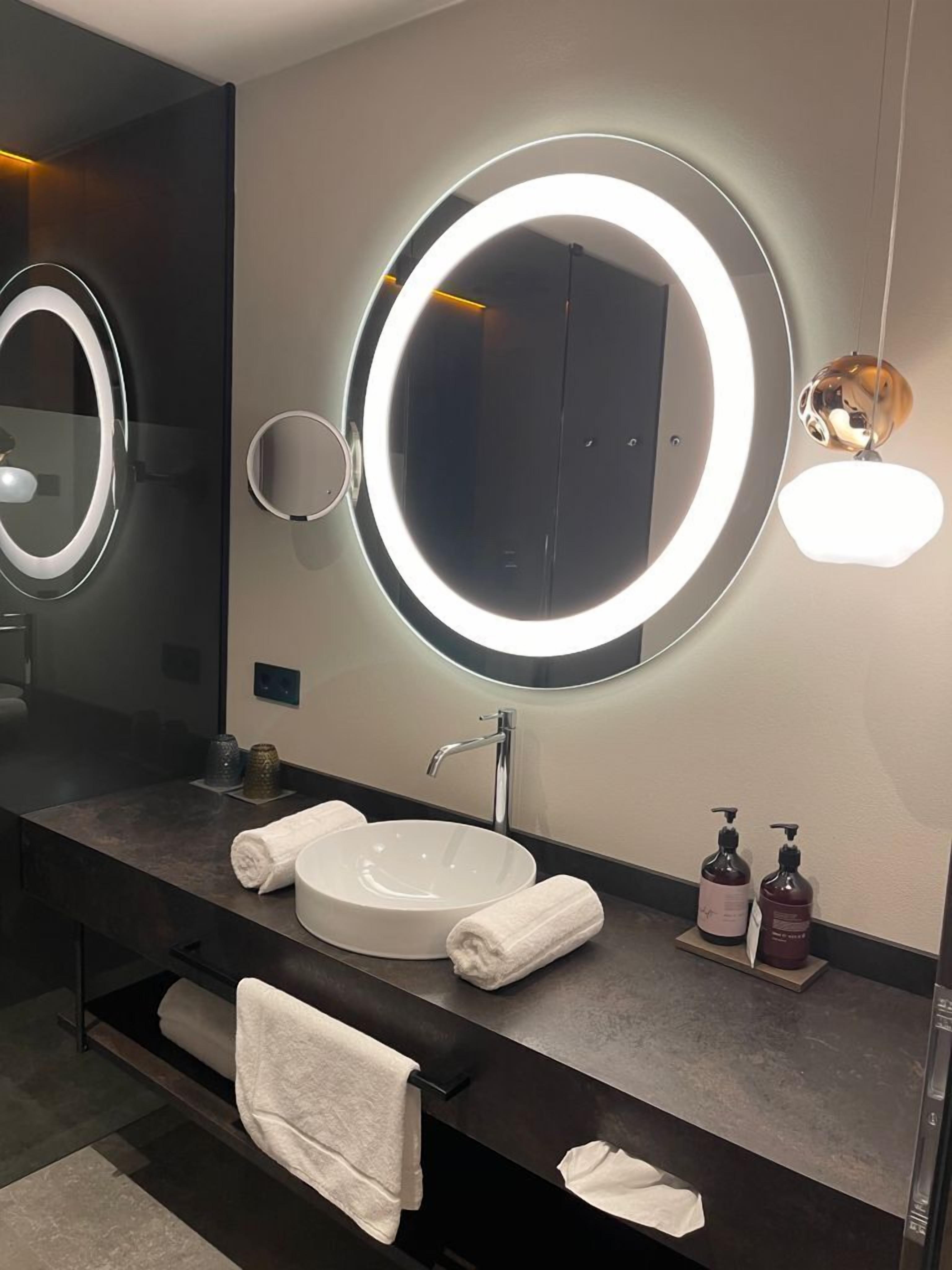 A modern bathroom with a large mirror, a round sink, and two towels on the counter.