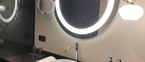 A modern bathroom with a large mirror, a round sink, and two towels on the counter.