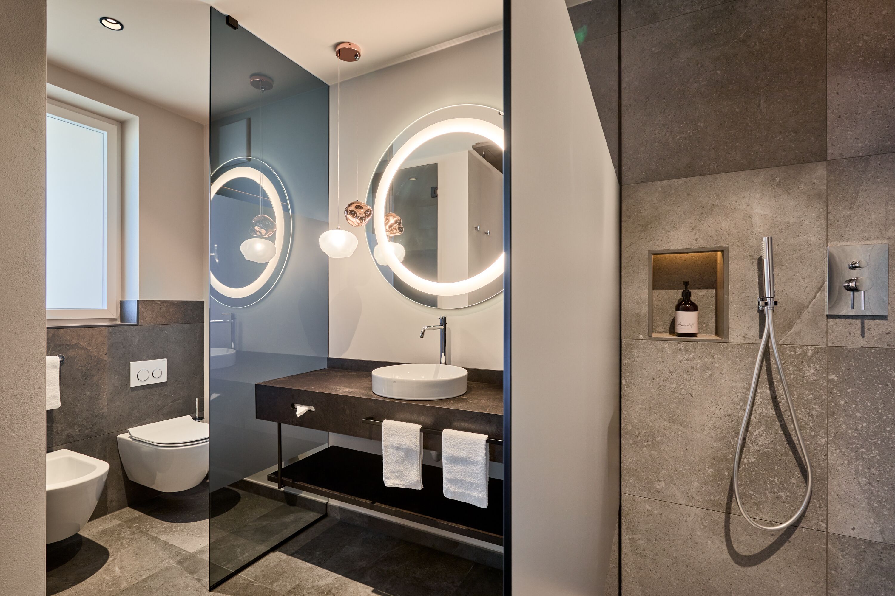 A modern bathroom with a round mirror, a sink, and a shower.
