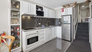 A compact kitchen with white cabinets, a microwave, a stove, a dishwasher, and a refrigerator. - Horizons 404 (Jindabyne)
