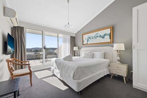 A hotel room with a large bed, a chair, a bedside table, a TV, and a view of the outdoors. - Horizons 404 (Jindabyne)