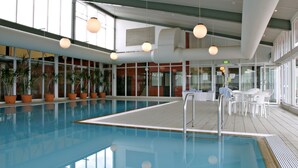 An indoor swimming pool with clear water, surrounded by potted plants, and a seating area with white chairs. - Horizons 404 (Jindabyne)