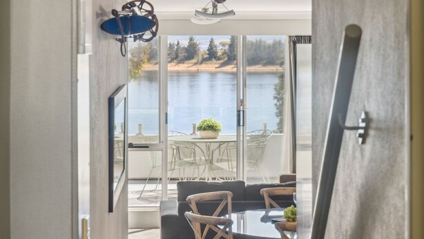 A room with a view of a lake, a dining area with a table and chairs, and a large window. - Horizons 404 (Jindabyne)