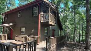 Une cabane dotée d’une terrasse en bois, d’un balcon et surplombant une forêt.
