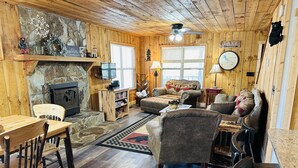 Un intérieur de chalet chaleureux avec une cheminée en pierre, des murs en bois, un canapé et un coin repas.