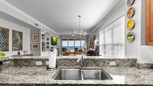 A modern kitchen with granite countertops, stainless steel sinks, and a view to the living area.