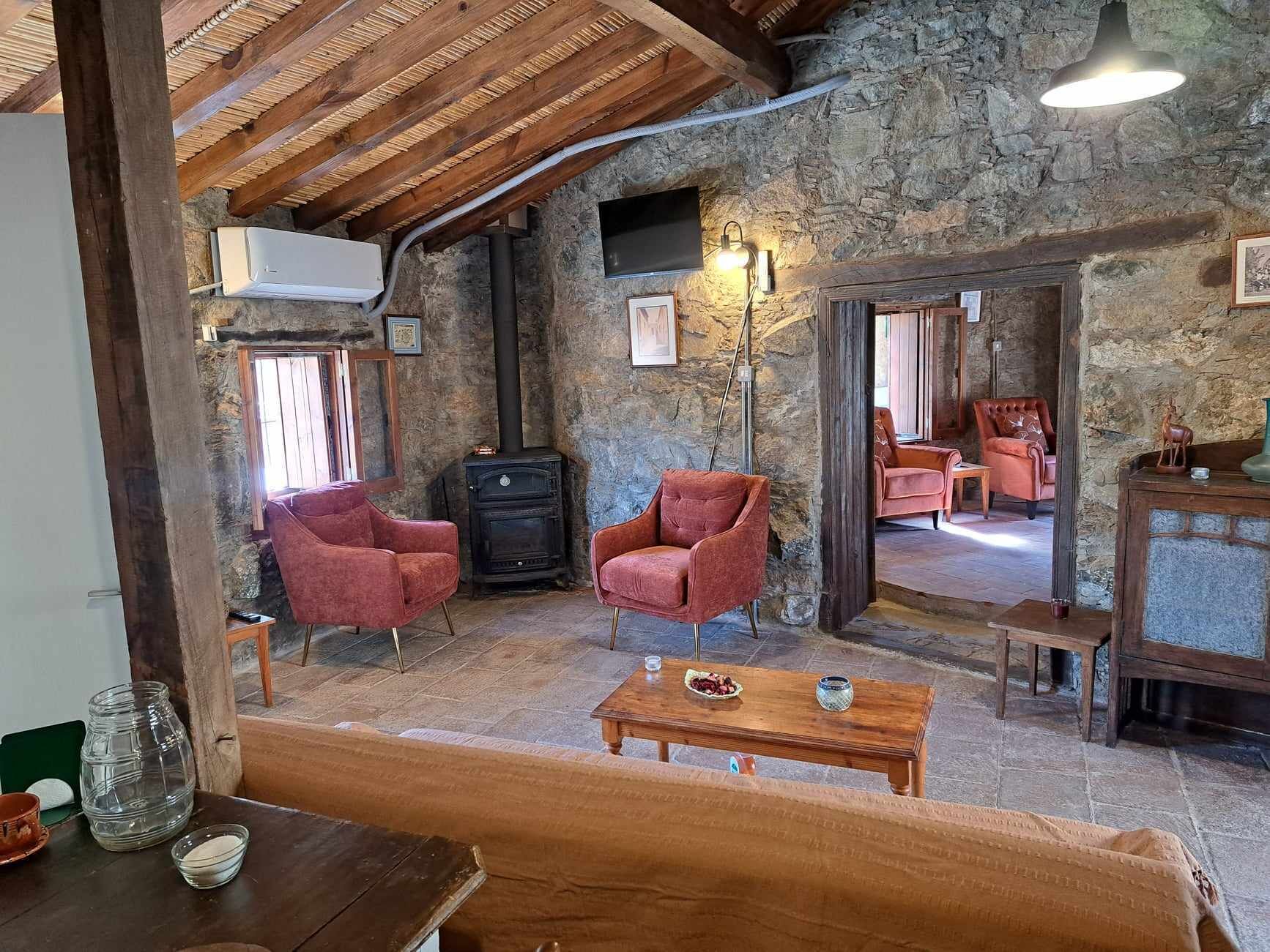 A rustic interior with stone walls, wooden beams, a fireplace, and seating areas.