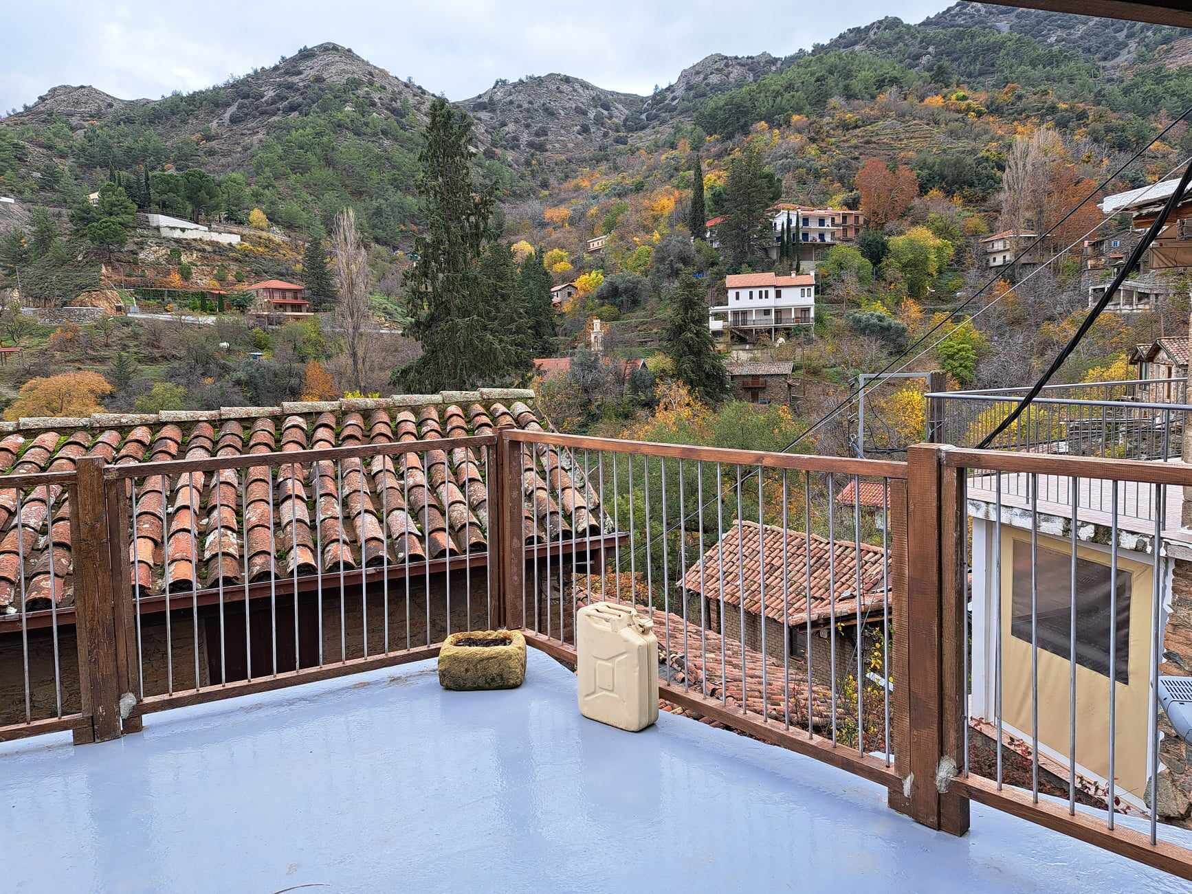 A balcony with a tiled roof, a wooden railing, and a view of a mountainous landscape with houses.