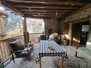 Un espace extérieur aménagé dans un style rustique, avec une table recouverte d’une nappe à carreaux, un sol en pierre et une vue sur les bâtiments environnants.