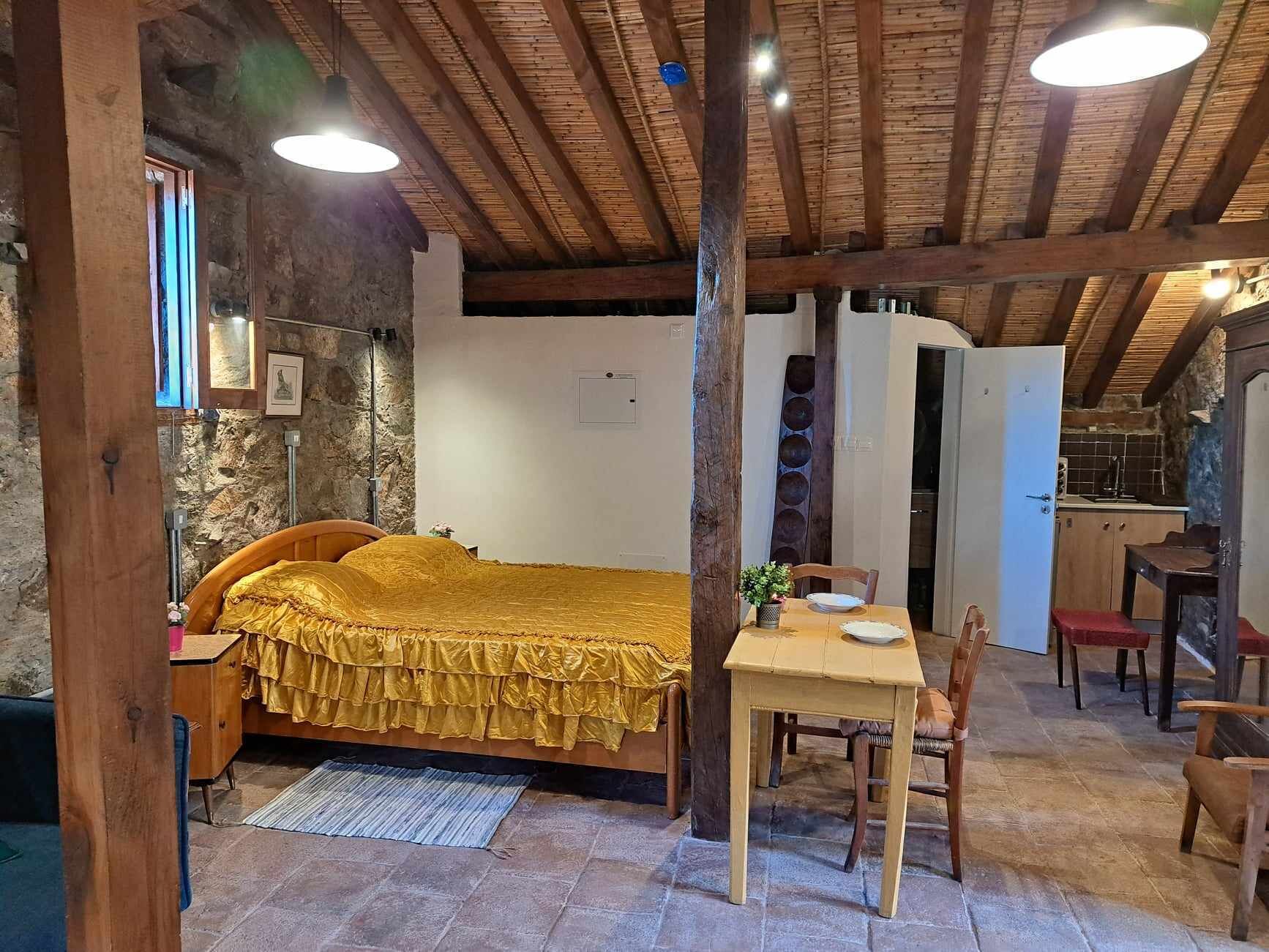 A rustic room with a bed, a dining table, and a kitchen area.
