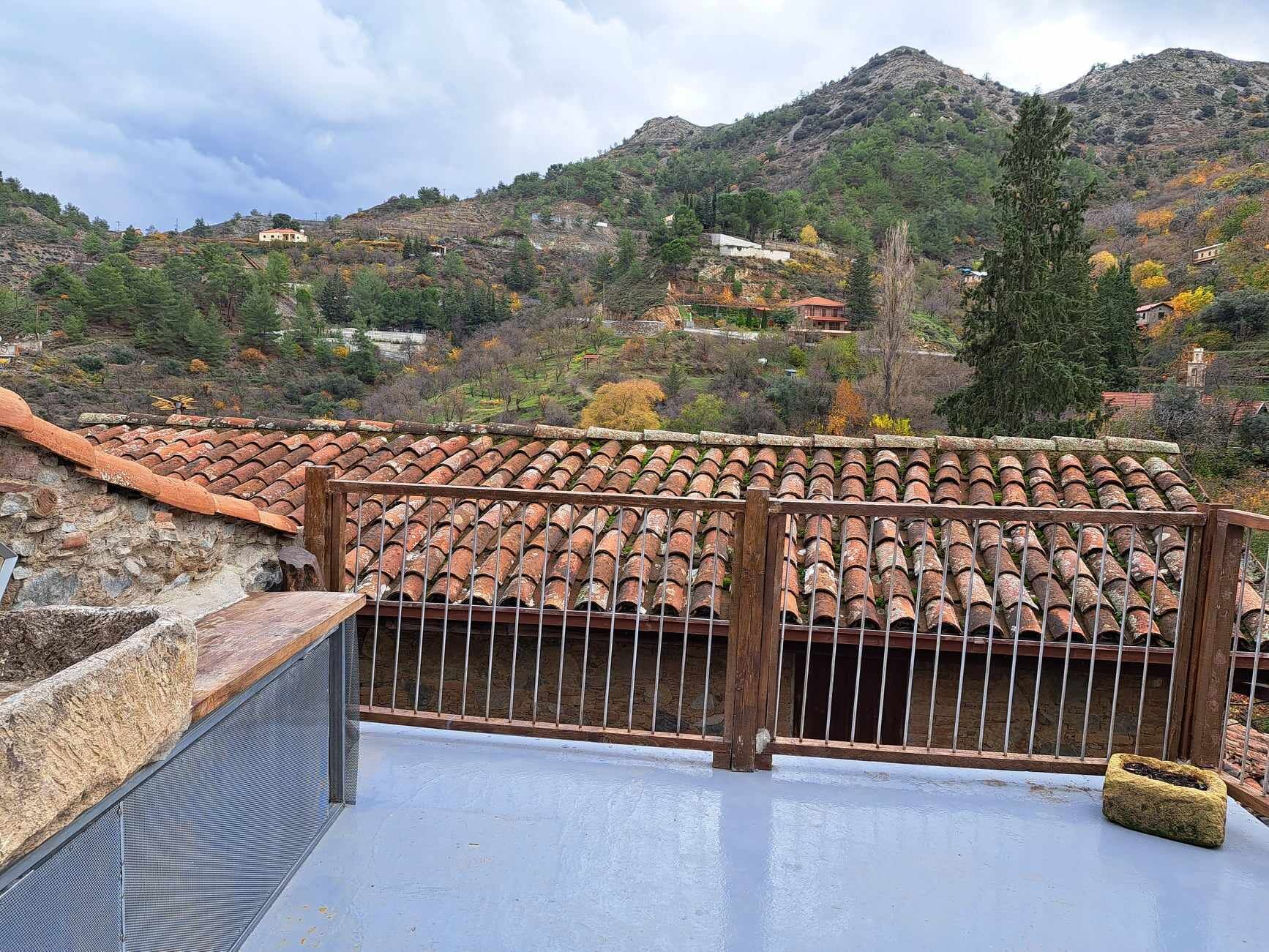 Una terraza en la azotea con baldosas de terracota, un muro de piedra y una barandilla de metal.