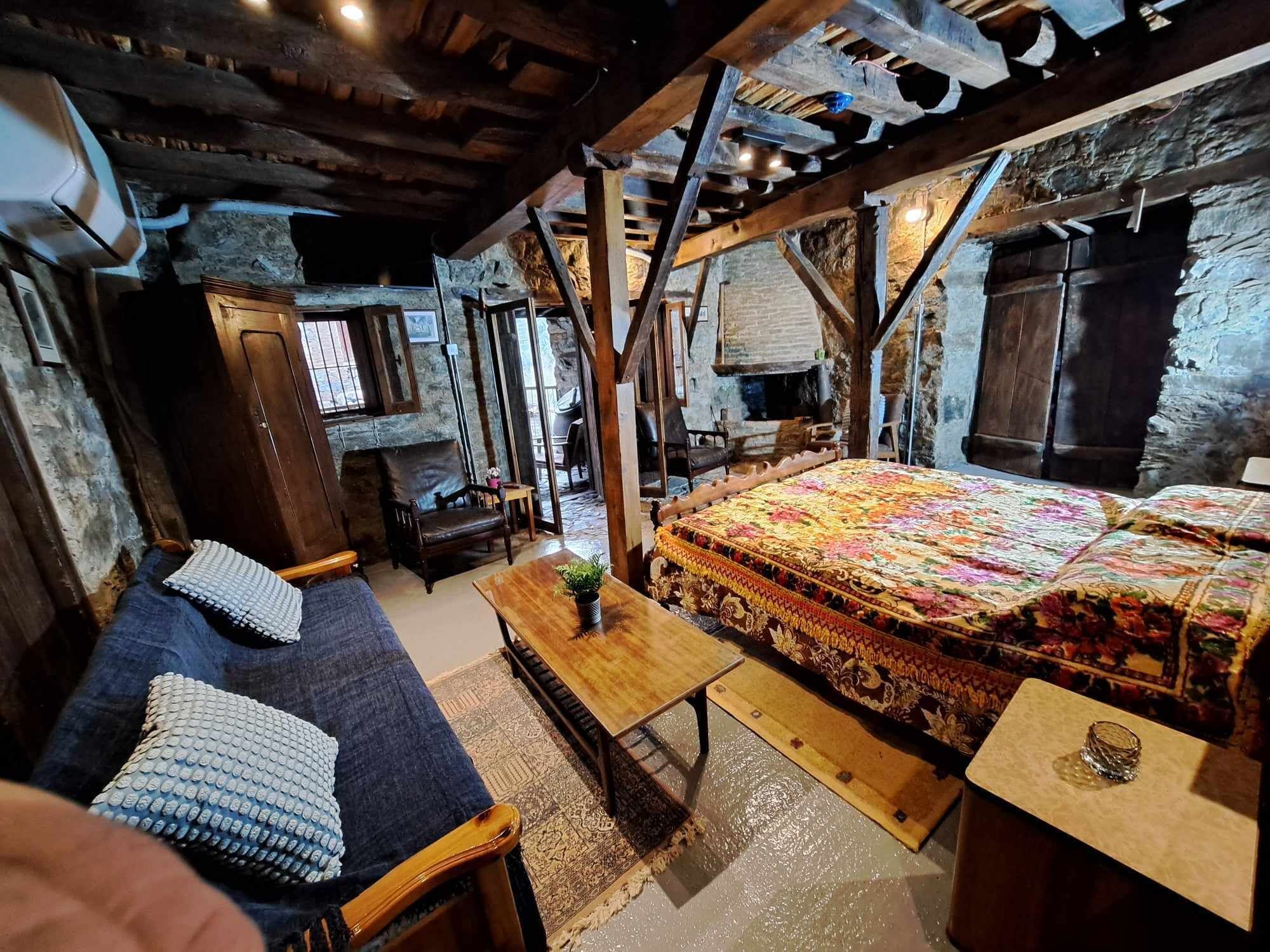 Una habitación rústica con una cama, un sofá, una mesa de madera y una pared de piedra.