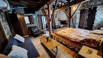 Una habitación rústica con una cama, un sofá, una mesa de madera y una pared de piedra.
