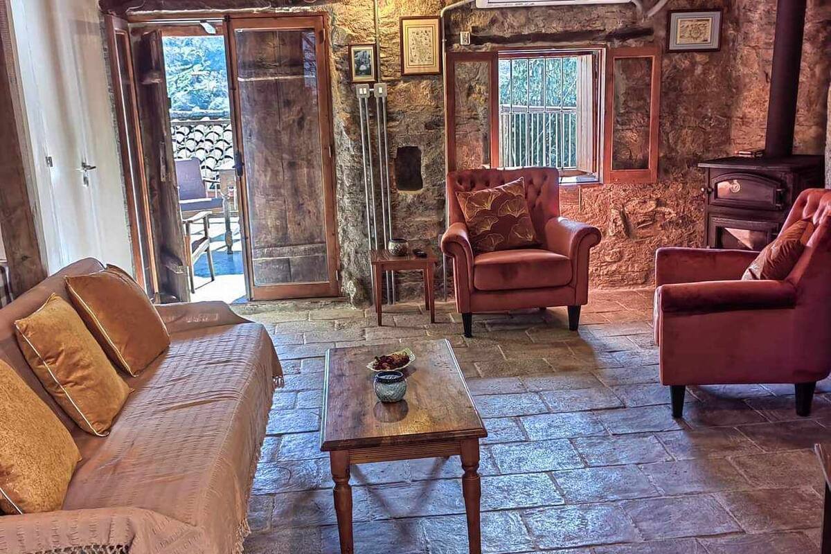 A rustic interior with a stone floor, a wooden table with a bowl, a sofa, and two armchairs.