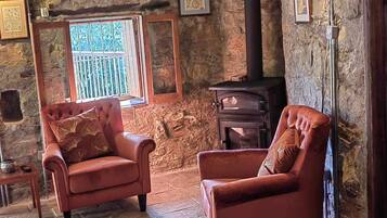 A cozy room with stone walls, a fireplace, and two leather armchairs.