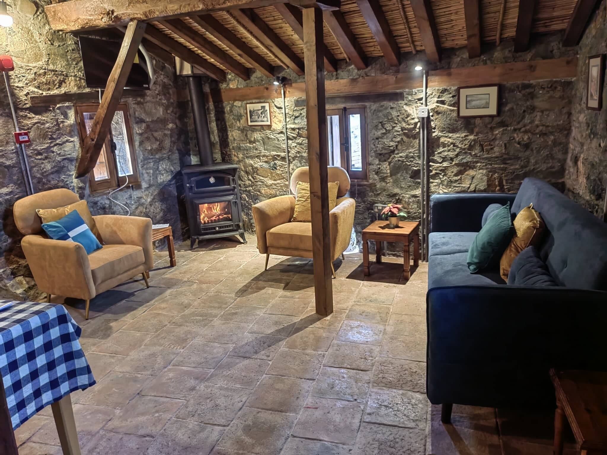 A cozy room with stone walls, a fireplace, and wooden beams. There are two sofas and a small table.