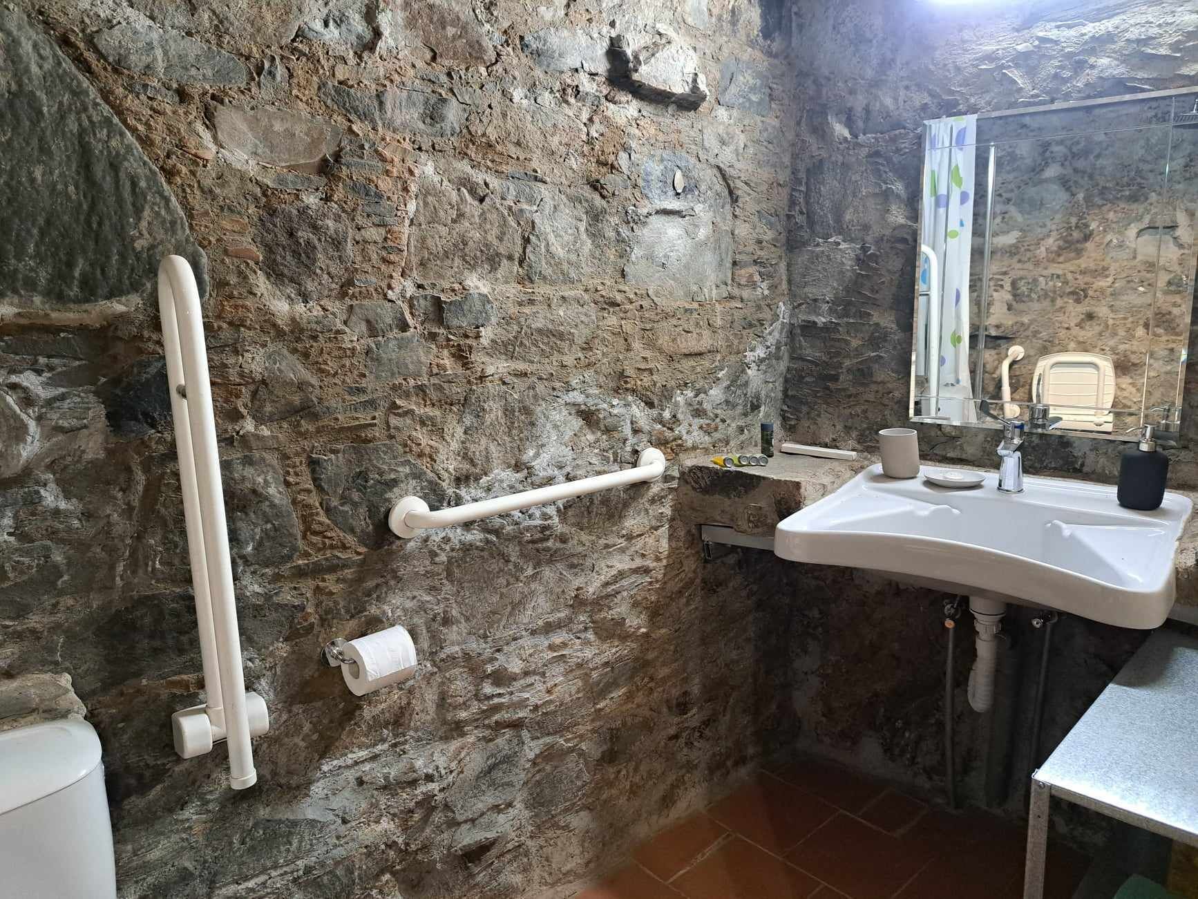 A bathroom with a stone wall, a white sink, a mirror, and a toilet.