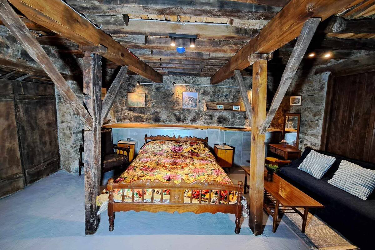 A rustic bedroom with a wooden bed, a stone wall, and a wooden staircase.