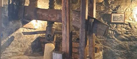 Una habitación rústica con paredes de piedra, un banco de piedra, vigas de madera y una lámpara colgante.