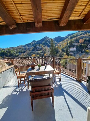 Une terrasse en bois avec une table et des chaises, offrant une vue sur un vignoble et des collines.