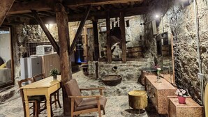 A rustic stone interior with wooden beams, a stone fireplace, a dining table, and a wooden chair. - PITHARIA (Askas)
