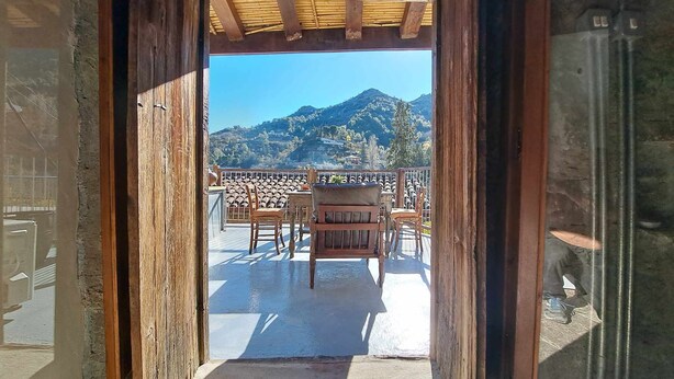 A wooden doorway leading to a balcony with a table and chairs, overlooking a mountainous landscape. - PITHARIA (Askas)