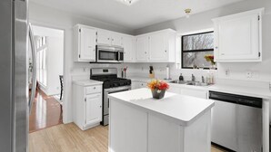 Una cocina moderna con muebles blancos, una isla central, electrodomésticos de acero inoxidable y una ventana con vistas.
