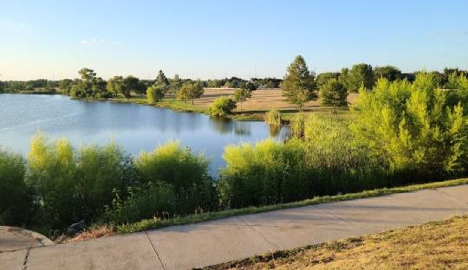 A serene lakeside view with a concrete pathway leading to the water.